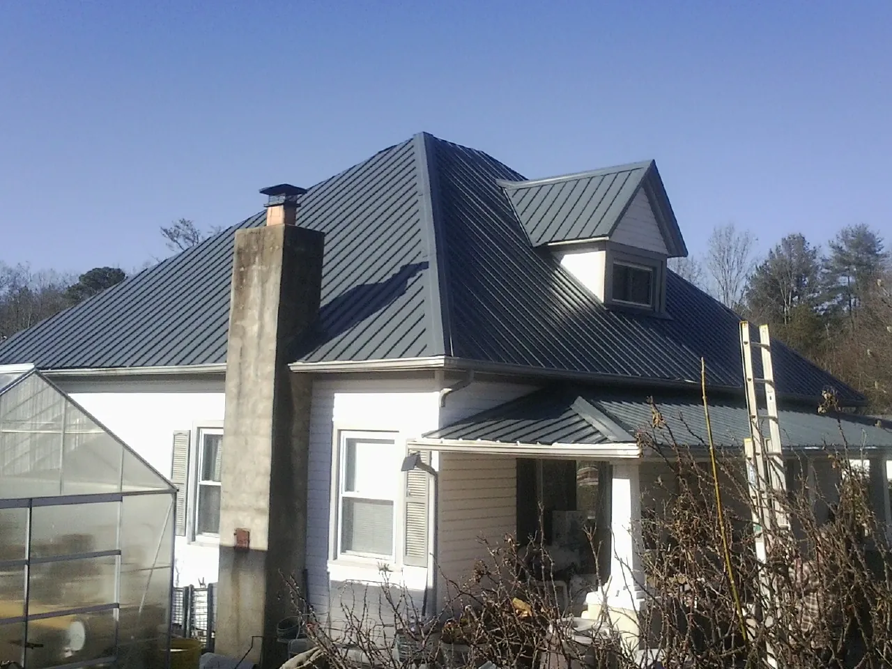 Dark blue standing seam metal roof on a white farmhouse with dormer — Slate & Tile Roof Repair by Roofing Brothers in Huntington Station
