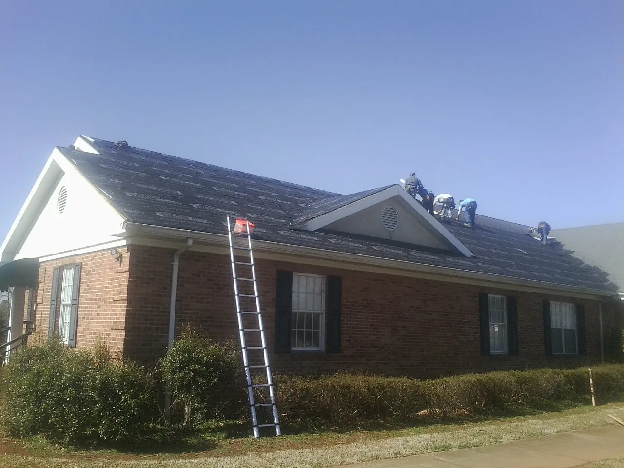 Crew tearing shingles off a brick ranch roof with a ladder set — Metal Roof Repair work by our crew in Huntington Station