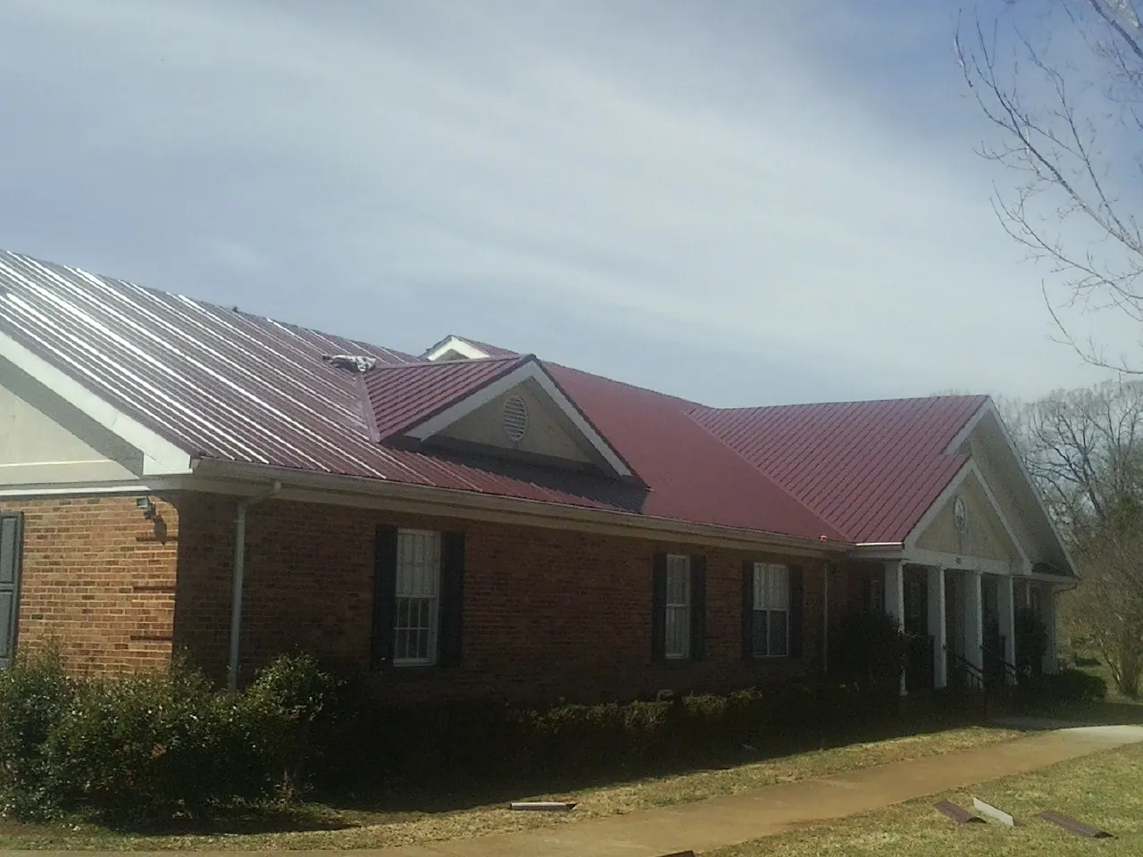 Red metal roof with gabled entries on a long brick building, from a Hail Damage Roof Repair job in Huntington Station