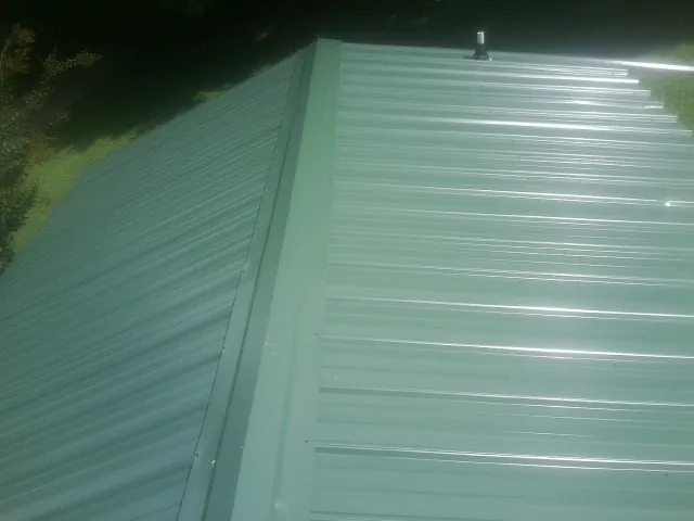 New green metal panels meeting at the ridge of a roof — Flat Roof Repair work by our crew in Huntington Station