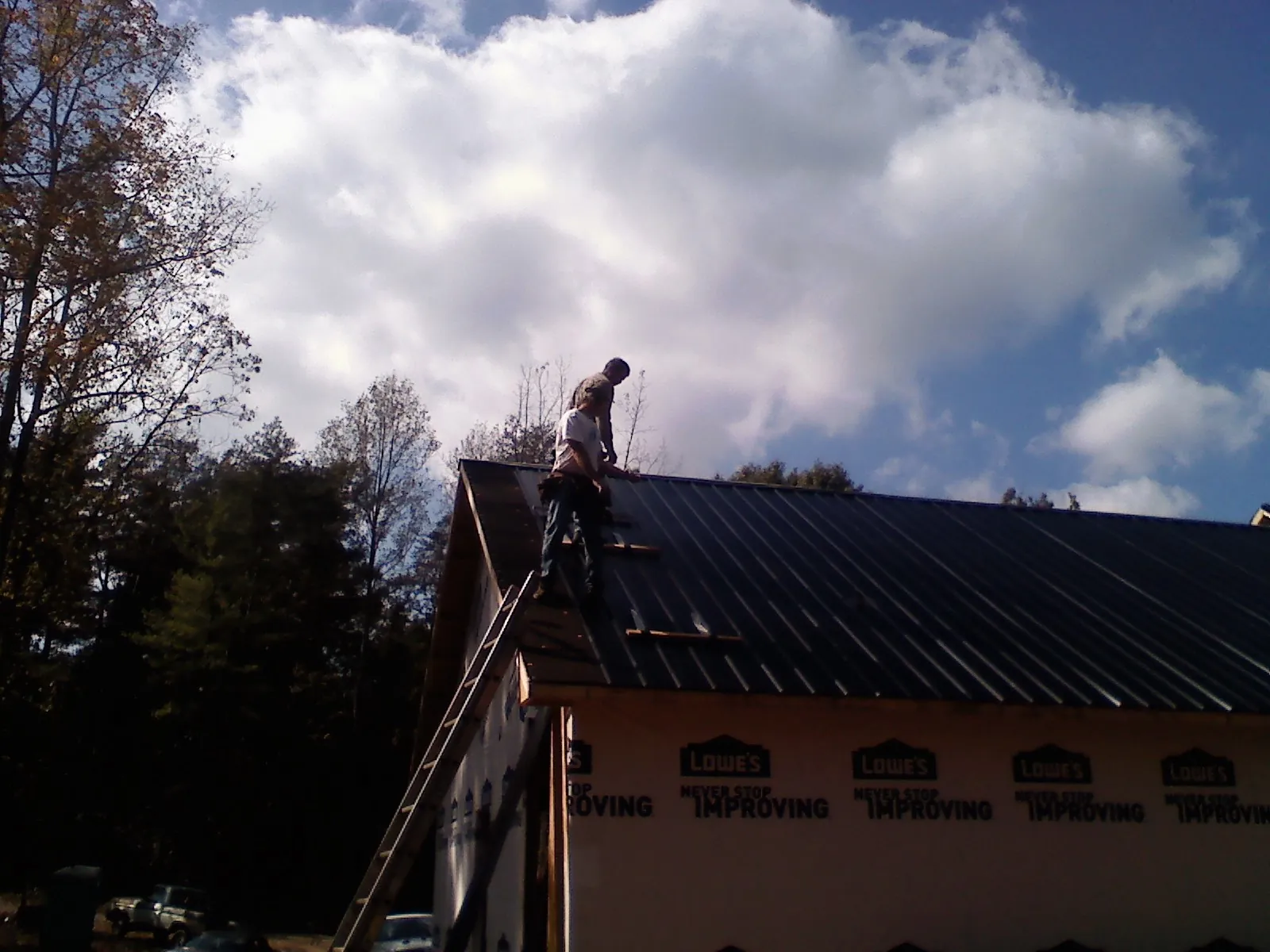 Roofer fastening dark metal panels high against a cloudy sky, from a Roof Inspection job in Huntington Station