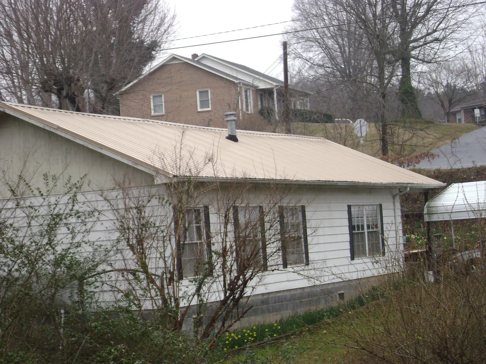 Tan metal roof on a white sided house set into a hillside — Commercial Roofing by Roofing Brothers in Huntington Station