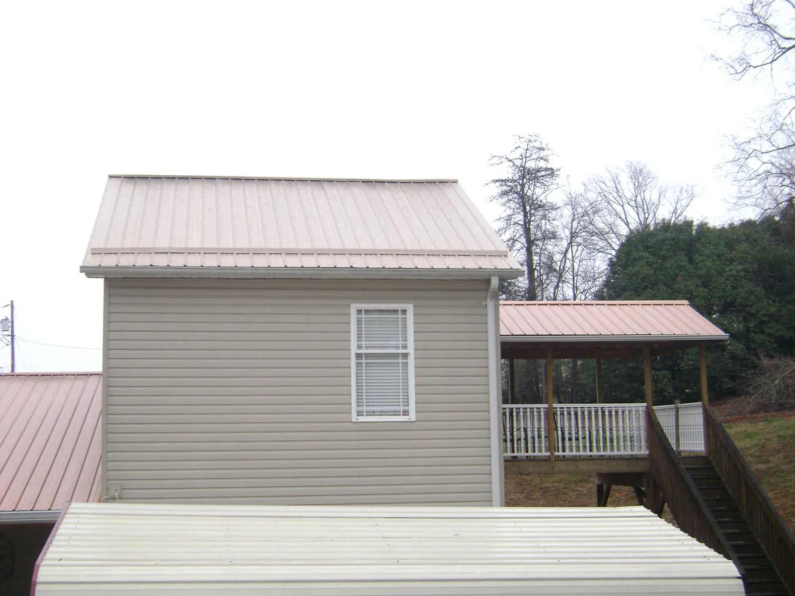 Tan metal roofs on a two story addition and attached porch, from a Roof Replacement job in Huntington Station